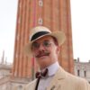 A man in a suit and hat stands in front of a tall tower