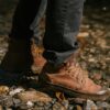 Crop anonymous person in brown boots and black jeans walking on stones near river bank