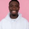 Positive African American male wearing white sweatshirt smiling widely against pink background and looking at camera