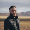 a man in a black jacket standing in a desert